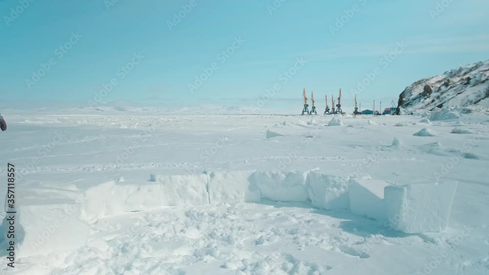 athletic tourist puts white snow block building igloo on frozen sea surface against hills under blue sky on sunny day athletic tourist puts white snow block building igloo on frozen sea surface against hills under blue sky on sunny day