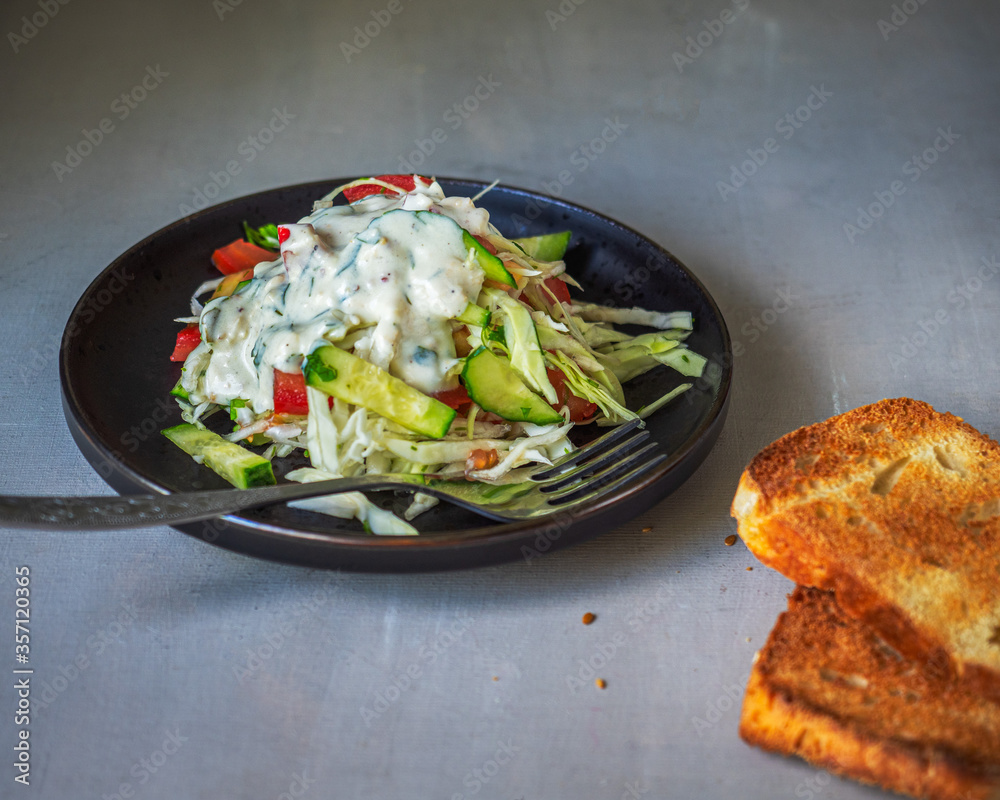 Light vegetable cabbage salad with tomatoes and cucumbers in a sauce on a black ceramic plate Light vegetable cabbage salad with tomatoes and cucumbers in a sauce on a black ceramic plate
