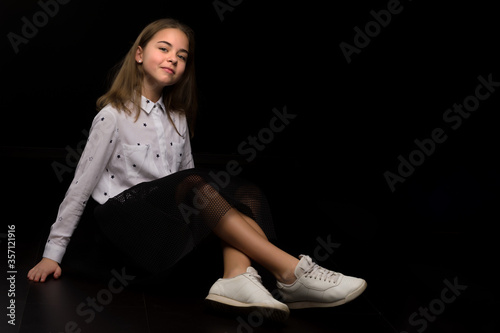 A little girl is sitting in the studio on the floor on a black background.