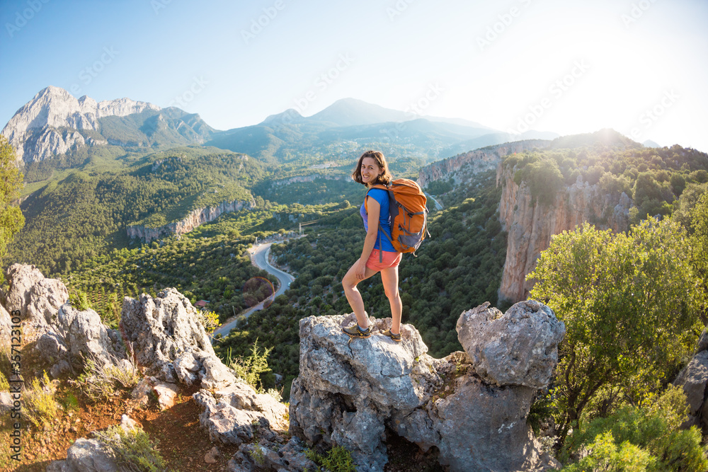 A woman with a backpack stands on top of a mountain and admires the beauty of a mountain valley.