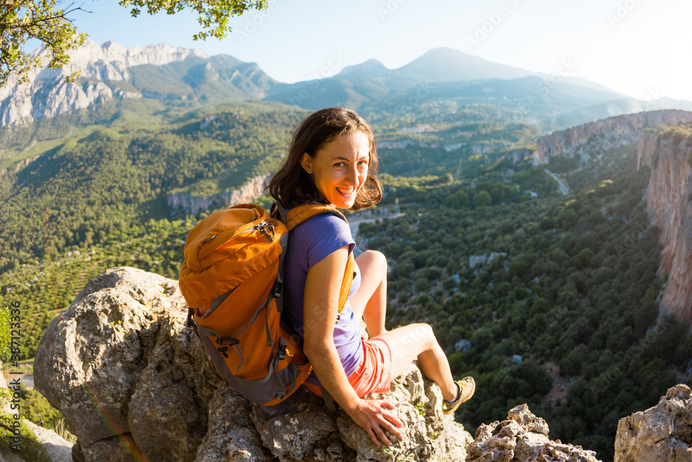 Naklejka premium A woman with a backpack sits on top of a mountain and admires the beauty of a mountain valley.