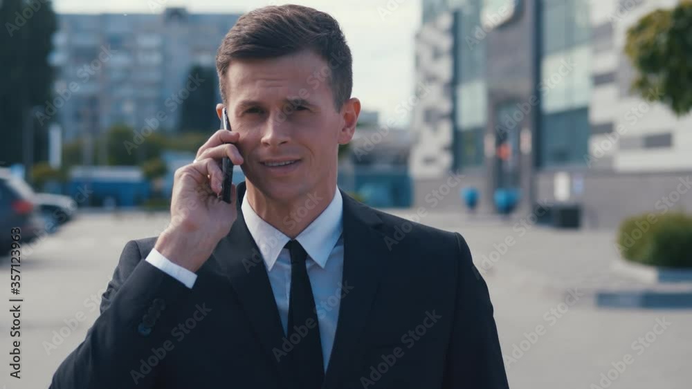 Portrait of confident businessman in classical suit talking on phone and walking in street. Young business man having business conversation. Portrait of confident businessman in classical suit talking on phone and walking in street. Young business man having business conversation.