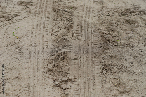 Imprints of car tires on a dirt country road in the light of the setting sun.