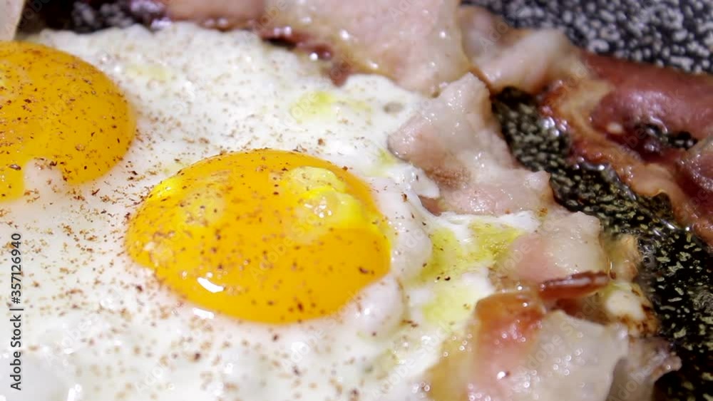 Cooking eggs and bacon in oil. Frying eggs for English breakfast. Delicious pepper poured. Cooking in a pan Cooking eggs and bacon in oil. Frying eggs for English breakfast. Delicious pepper poured. Cooking in a pan