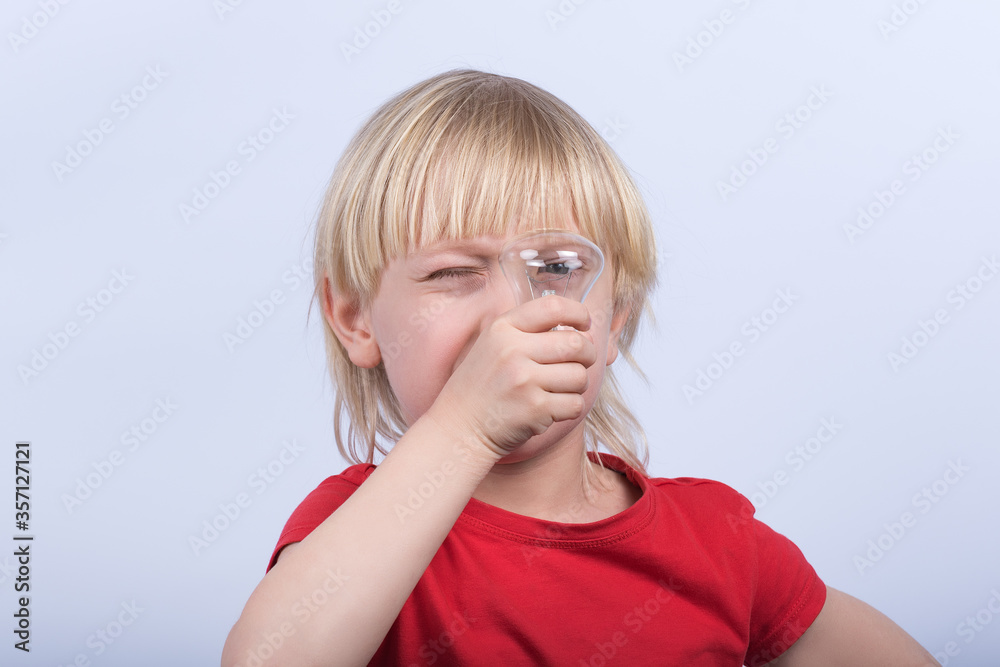 Fair-haired boy looking through the bulb. Portrait of child with incandescent lamp in hands on white background Fair-haired boy looking through the bulb. Portrait of child with incandescent lamp in hands on white background