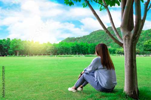 Asian woman sitting under a tree in the park. Sit and rest comfortably on your vacation..