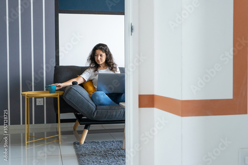 Beautiful girl sitting with a laptop on a sofa in a stylish room. Work from home. Work atmosphere in a good mood