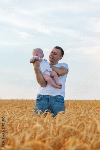 Young father playing with baby in middle of wheat field. Weekend in countryside. Vertical frame photo