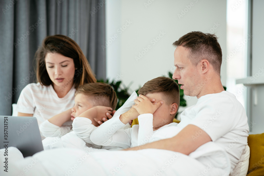 Young family watching movie on lap top. Beautiful parents with kids enjoying at home.