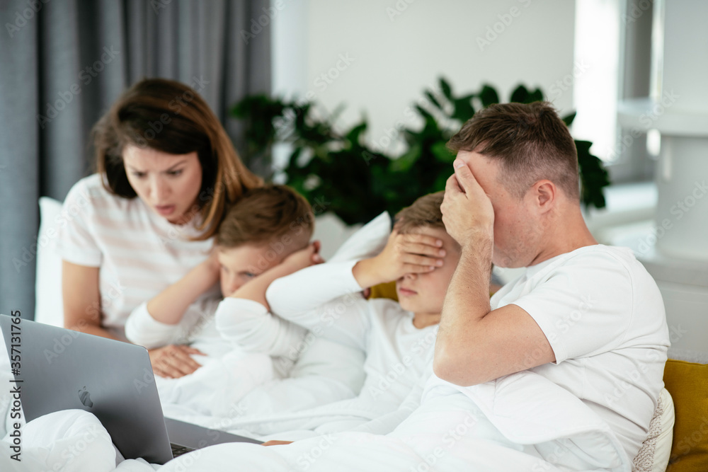 Young family watching movie on lap top. Beautiful parents with kids enjoying at home.