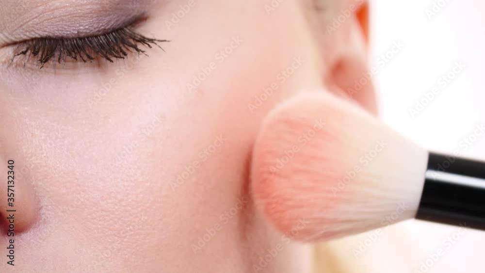 Woman face painting. Makeup artist applying blush with brush to model cheek. Cosmetic beauty procedures and makeover concept. Slow motion Woman face painting. Makeup artist applying blush with brush to model cheek. Cosmetic beauty procedures and makeover concept. Slow motion