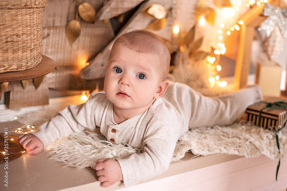 Fototapeta premium A small baby in light clothing lies on the background of the Christmas decor.