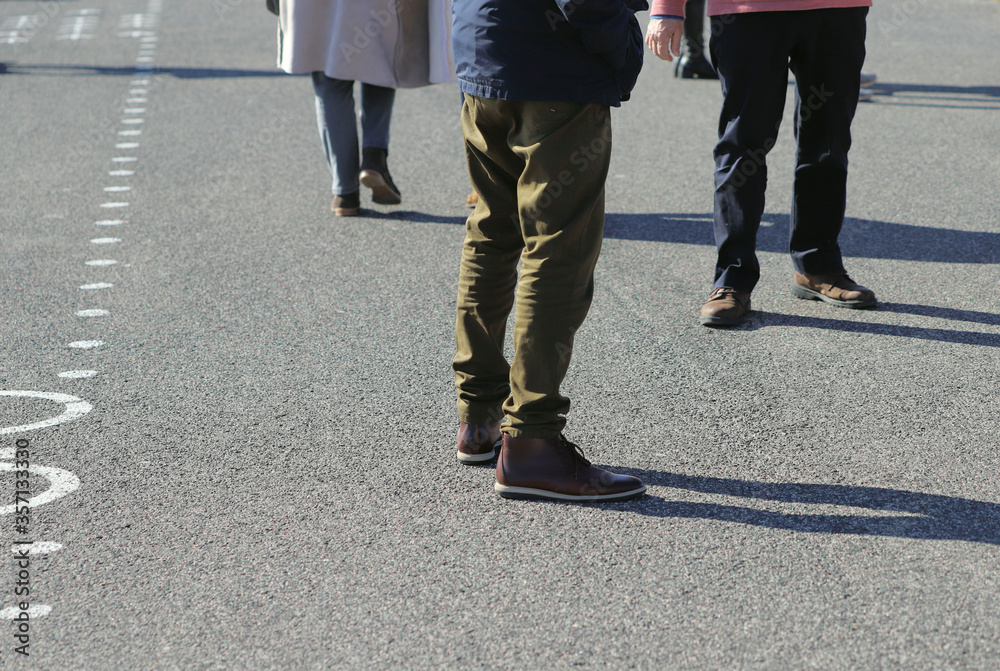 Obraz premium Men and women walking on a city street. Male and female legs in trousers. The concept of distance under quarantine of a coronovirus. Spring men's fashion.