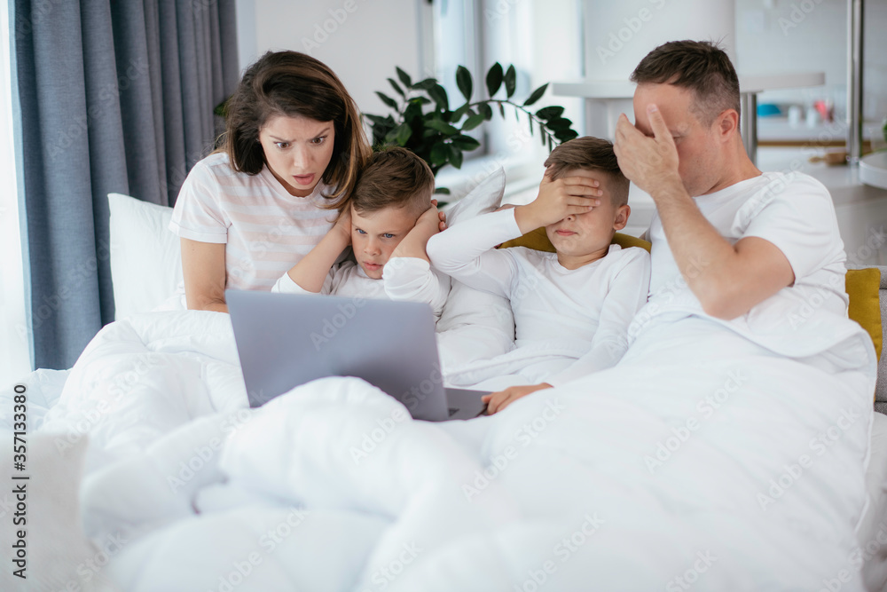 Obraz premium Beautiful parents with kids enjoying at home. Young family watching movie on lap top.