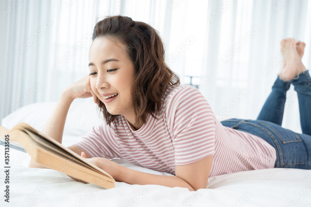 An Asian woman is lying reading in bed with a kitten. concept life style, pets, stay at home, new normal, mental state, interior decoration, background An Asian woman is lying reading in bed with a kitten. concept life style, pets, stay at home, new normal, mental state, interior decoration, background