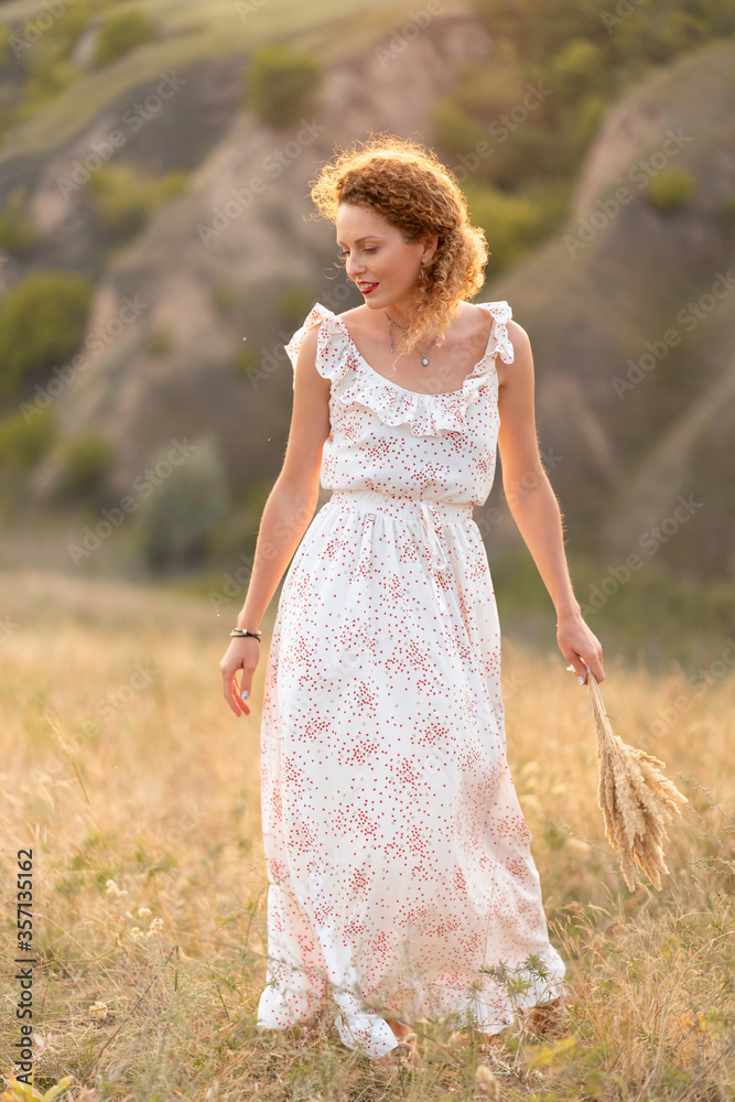 Beautiful tender girl in a white sundress walks at sunset in a field with a spikelet bouquet. Beautiful tender girl in a white sundress walks at sunset in a field with a spikelet bouquet.