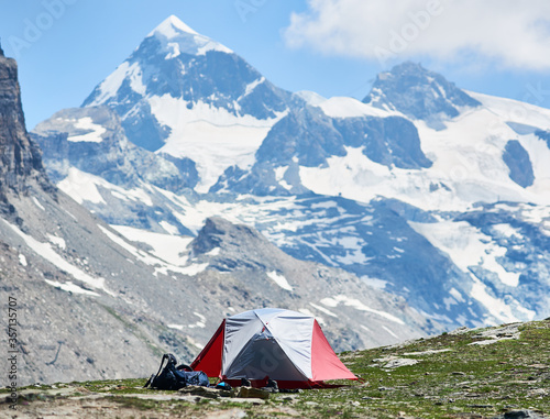 View of mountain valley with tourist tent and hiker belongings. Picturesque scenery of camp tent with majestic rocky hills and peak on background. Concept of travelling, camping and beauty of nature.