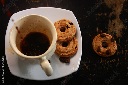 the process of pouring espresso on a white ceramic mug with some diet biscuits, suitable for coffee connoisseurs who don't want to consume a lot of calories from regular biscuits