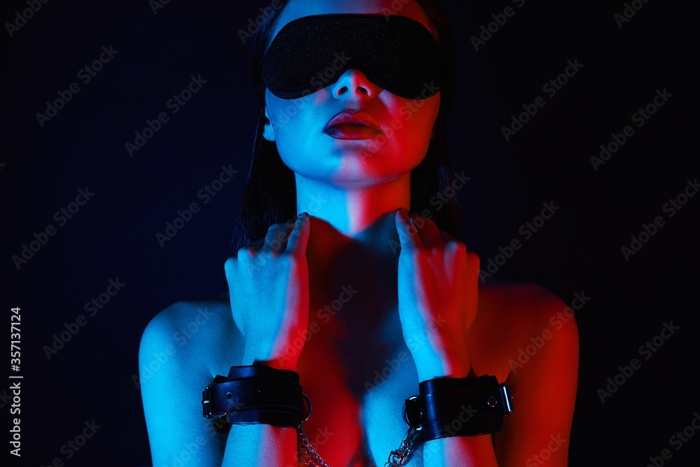 Girl in handcuffs and mask. in color lights. tied hands and