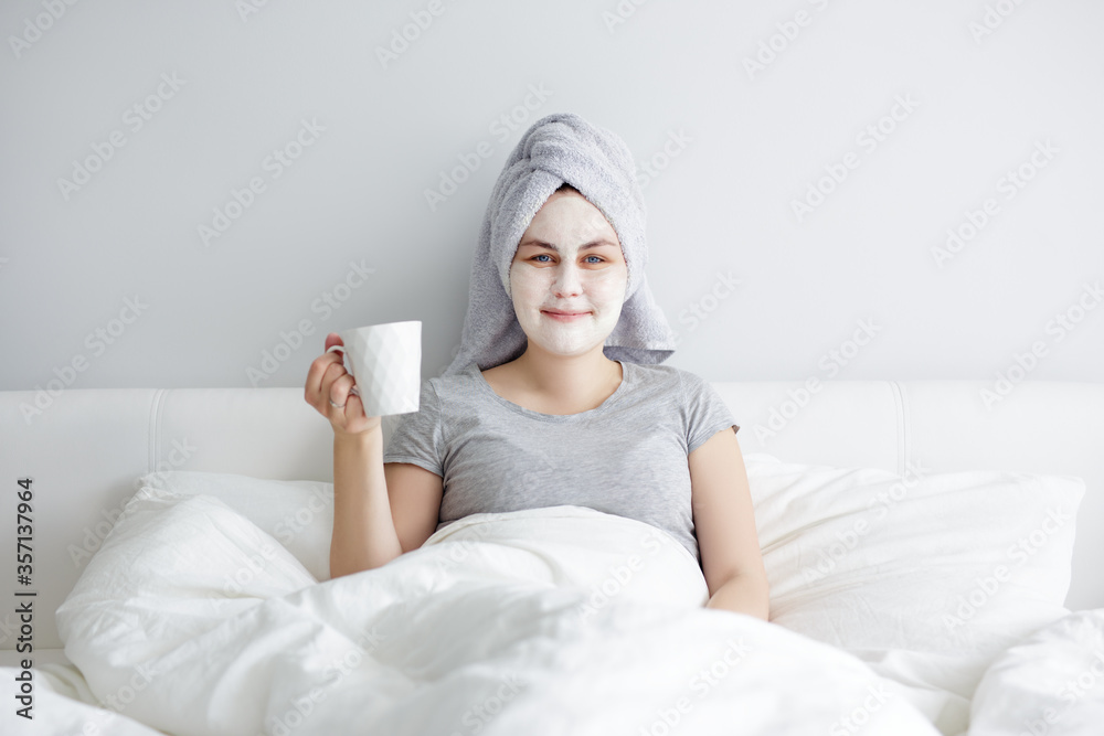 woman applying facial mask and drinking coffee in bed woman applying facial mask and drinking coffee in bed