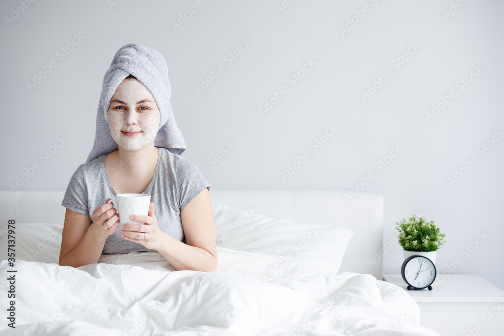 skin care concept - woman applying facial mask and drinking coffee in bed, copy space over white wall skin care concept - woman applying facial mask and drinking coffee in bed, copy space over white wall