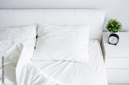 Foto top view of empty unmade bed with white blanket and two pillows, bedside table w
