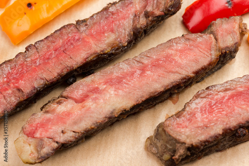 Grilled beef steak, cut into pieces on cutting board with red and yellow pepper.