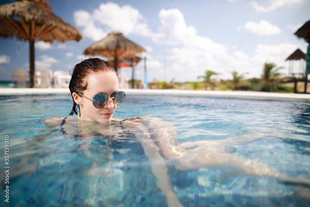 Close up view portrait of beauty caucasian woman with sunglasses in swimming pool enjoying vacation holidays at luxurious beachfront hotel resort and tropical landscape.
