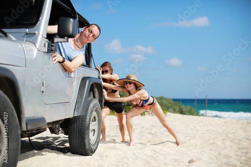 Wallpaper Mural The car stuck in the sand.Two beauty and sexy women in bikini  pushing a off road car near sea on beach while man is emboldening them.Transportation,teamwork,funny concept. Torontodigital.ca