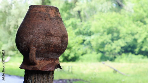 Old brown broken clay jug on a wooden fence in the countryside. Copy space. Pot on an old village fence