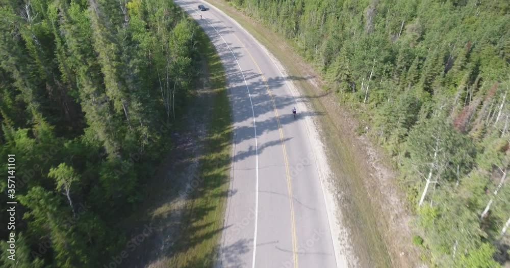 Drone flying over road with cyclist racing below. Road curves to the left, drone continues to fly over and tilts up to reveal more of the road ahead.