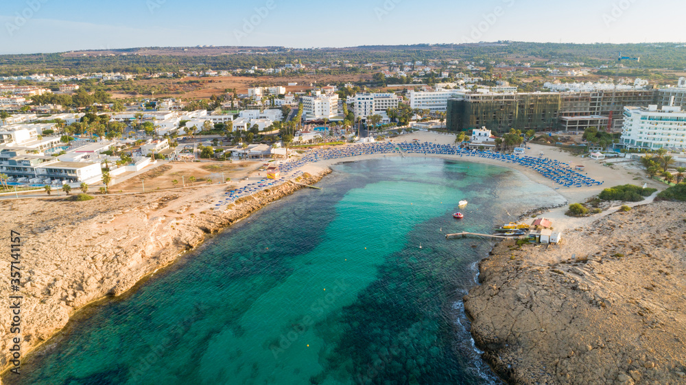 Aerial bird's eye view of Vathia Gonia beach, Ayia Napa, Famagusta, Cyprus. The landmark tourist attraction rocky bay at sunrise with golden sand, sunbeds, sea restaurants in Agia Napa, from above.