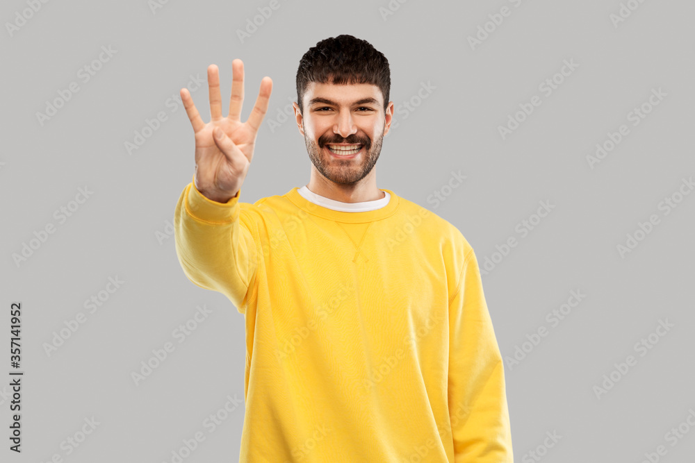 count and people concept - happy smiling young man in yellow sweatshirt showing three fingers over grey background