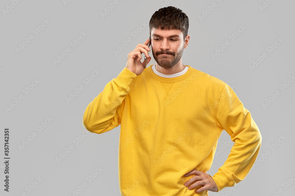 technology and people concept - puzzled young man in yellow sweatshirt calling on smartphone over grey background technology and people concept - puzzled young man in yellow sweatshirt calling on smartphone over grey background