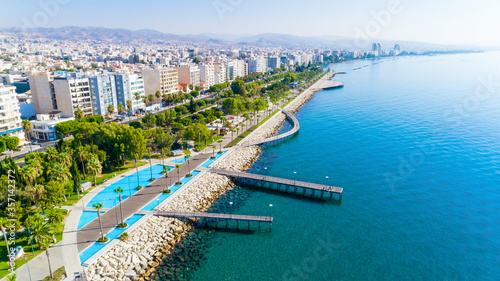 Aerial view of Molos Promenade park on coast of Limassol city centre,Cyprus. Bird's eye view of the jetty, beachfront walk path, palm trees, Mediterranean sea, piers, urban skyline and port from above