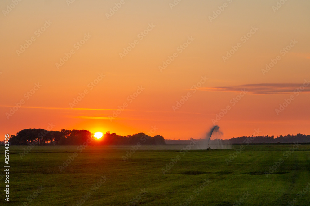 Evening hours in the Netherlands, the farmer irrigates his land and a setting sun, province of Friesland Evening hours in the Netherlands, the farmer irrigates his land and a setting sun, province of Friesland