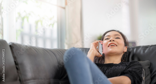 Happy young asian woman using mobile phone while sitting a couch at home