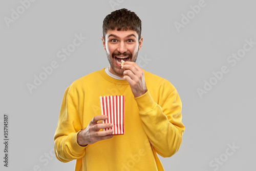 fast food and people concept - smiling young man in yellow sweatshirt eating popcorn over grey background