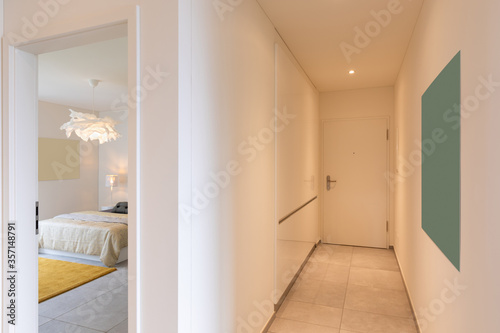 Interior of a long corridor of an apartment. At the bottom a closed door