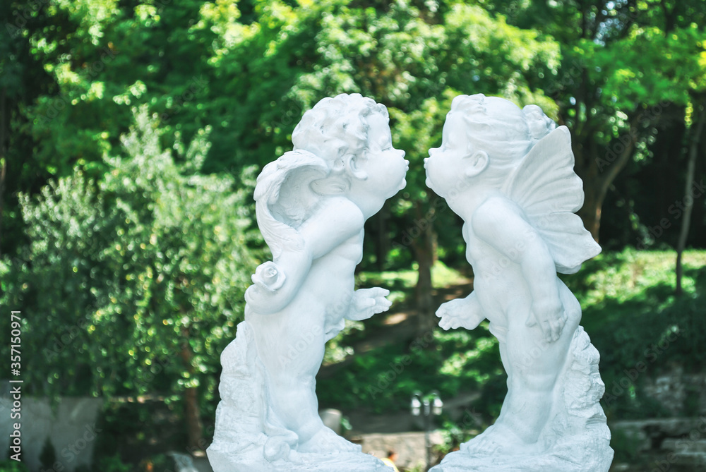 Obraz premium Figurine of kissing cupid boy and fairy girl in summer garden