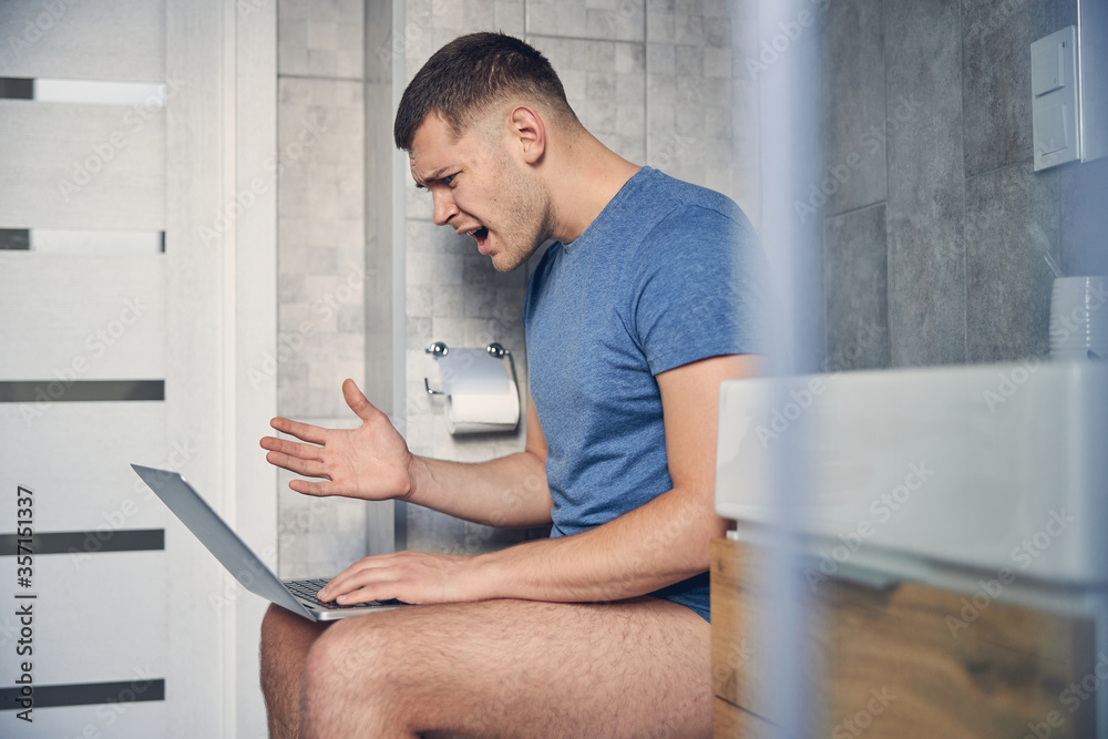 Young brunette male on a toilet with laptop