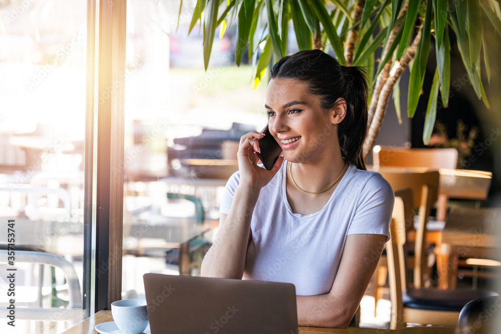 Young charming woman calling with cell telephone while sitting alone in coffee shop during free time, attractive female with cute smile having talking conversation with mobile phone while rest in bar
