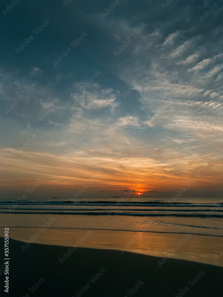 Dawn on the sea with a view of the horizon, colorful sky from sun rays, clouds on a blue sky, Vertical frame