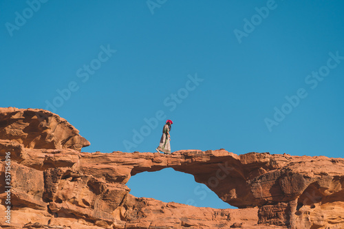 Young Asian traveller walking on natural rock bridge in Wadi Rum desert in Jordan, Arab, Asia