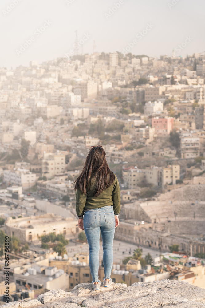 Young Asian woman traveller standing on stone and enjoying top view of Amman capital city of Jordan, Arab