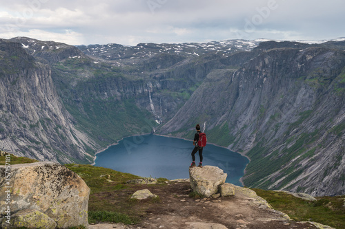 Asian woman traveller with backpack standing on rock and enjoying landscape of mountains and lake in Trolltunga mountain cliff trail, Odda town, Norway, Scandinavia