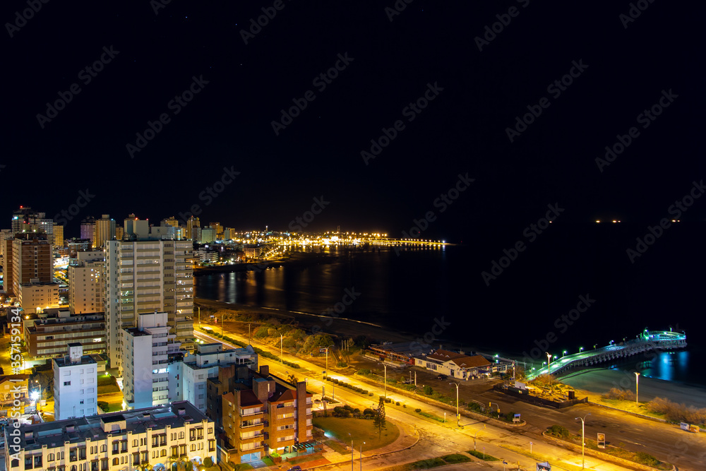 Long exposure panoramic view of the quiet beach, the calm water, the empty streets and the illuminated harbor seen from a hotel room balcony on a clear dark night at coast city Punta Del Este, Uruguay