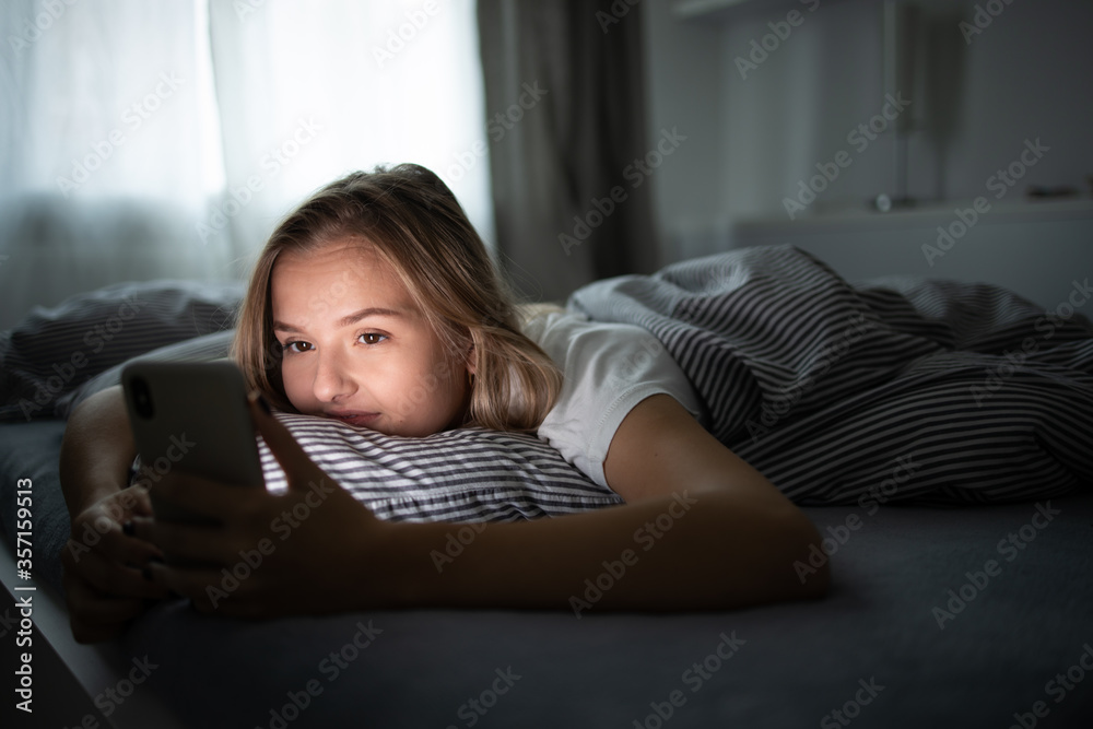Pretty, young woman using her smart phone in bed Smartphone in Bed Mobile/smartphone  Addiction Concept.