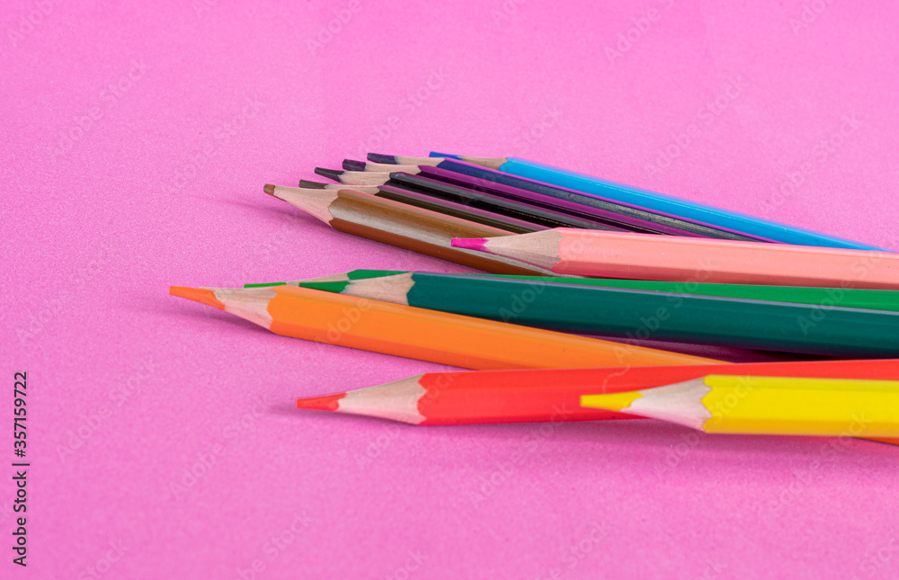 Multi-colored pencils are scattered on a bright pink background. School supplies. Foreground Defocus Multi-colored pencils are scattered on a bright pink background. School supplies. Foreground Defocus