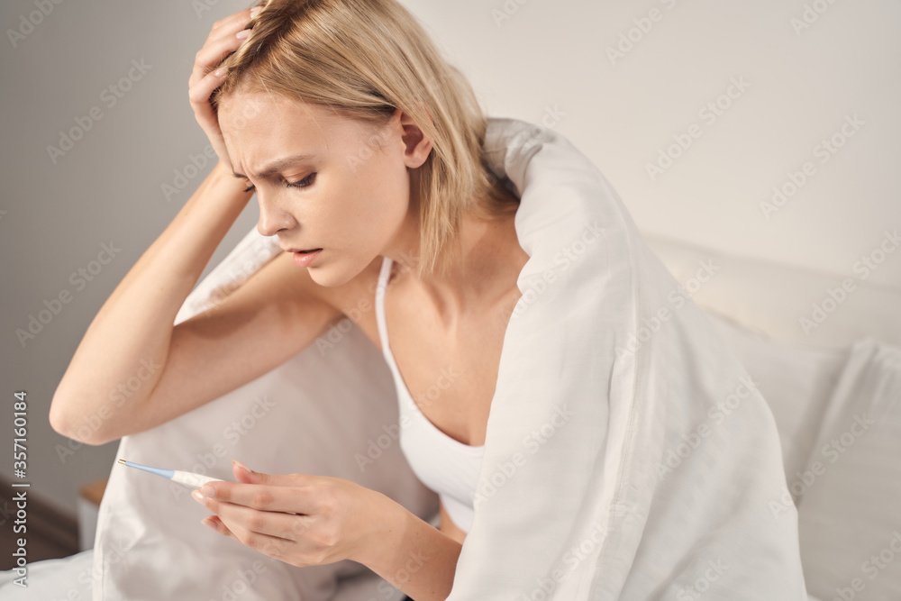 Frustrated lady staring at her digital thermometer Frustrated lady staring at her digital thermometer